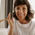 Kobieta nakłada krem z filtrem na twarz, aby chronić ją przed słońcem.